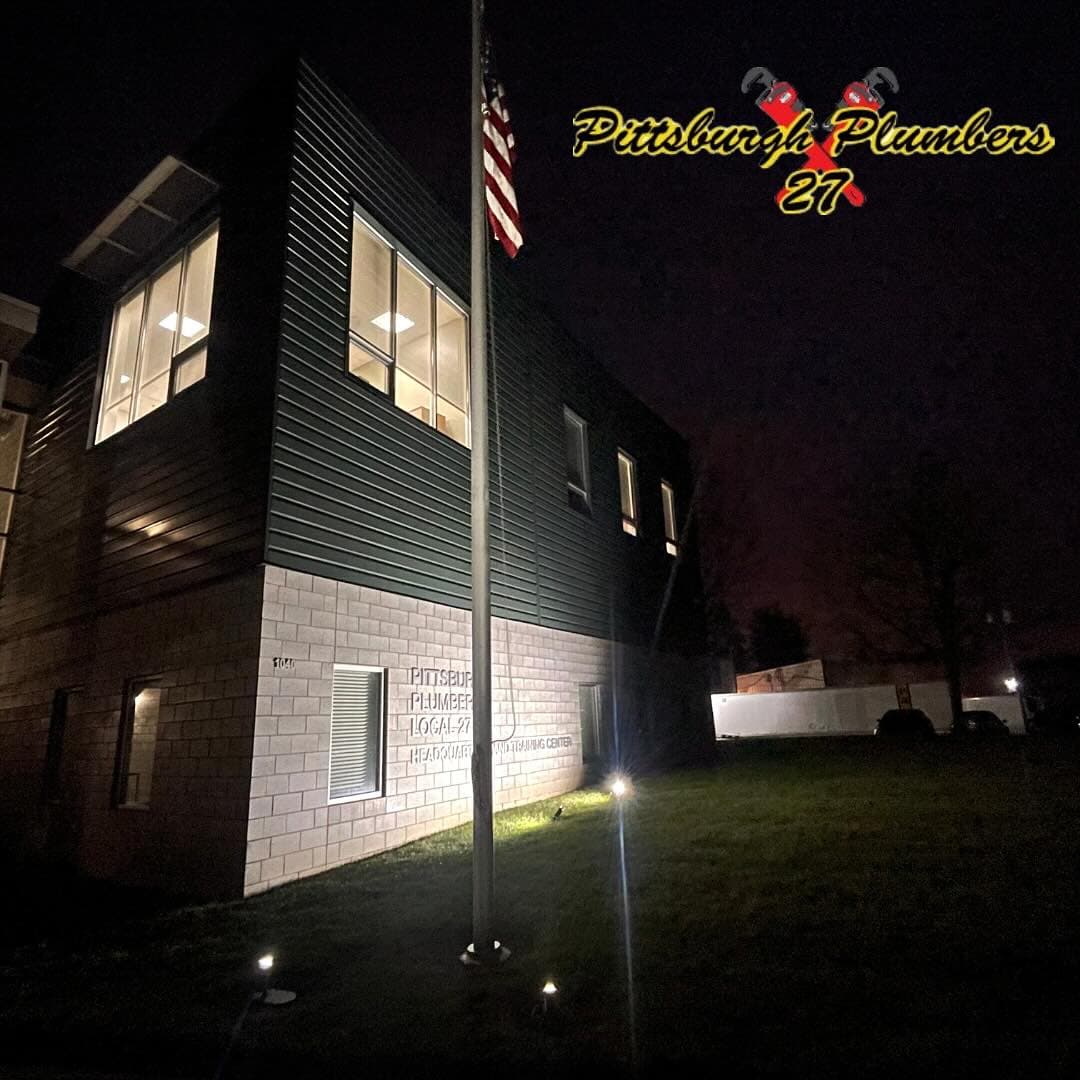 The UA Local 27 union hall at night with the American flag lit at the entrance — Coraopolis, PA.