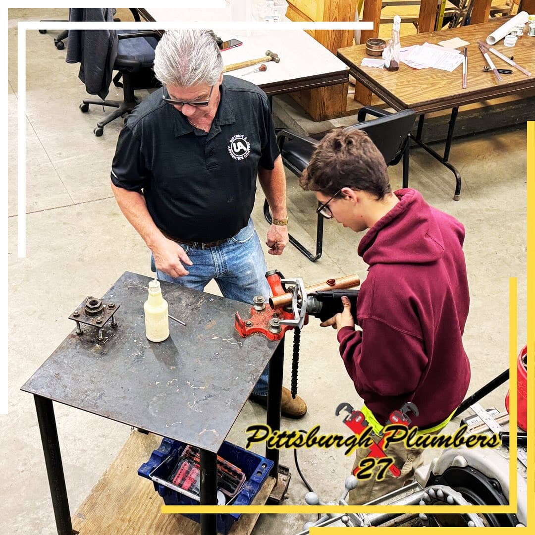 A veteran UA Local 27 journeyman teaching a young apprentice to thread pipe.